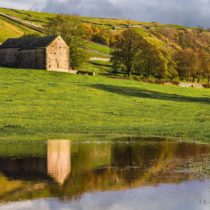 Traditional stone barn reflected in a flooded field near Kettlewell, Wharfedale, Yorkshire Dales, England. EL013