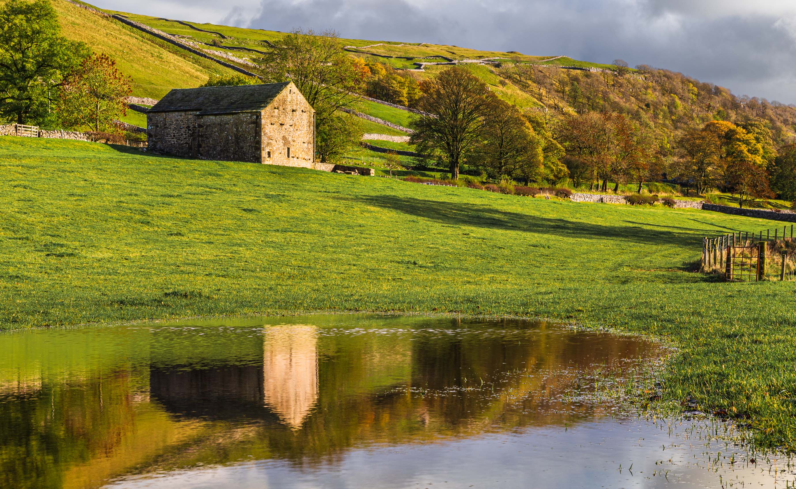 Traditional stone barn reflected in a flooded field near Kettlewell, Wharfedale, Yorkshire Dales, England. EL013