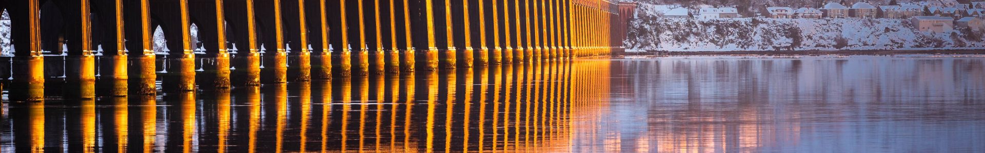 The central section of the Tay Railway Bridge passing across a flat-calm Tay at sunset, Dundee, Scotland. DD130